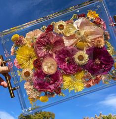 a person holding up a glass block with flowers in it and the sky behind them