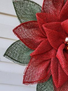 a red mesh flower with green leaves on the side of a house, in front of a white wall