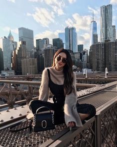 a woman sitting on top of a metal fence next to a tall building with a city skyline in the background