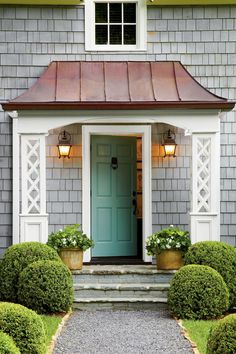 a blue front door with two potted plants on the steps and one green door