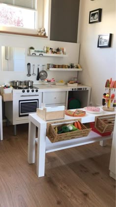 a small kitchen with white appliances and wooden flooring in the center, along with various items on the table