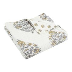 the white and gold floral print blanket is folded up on top of a bed sheet