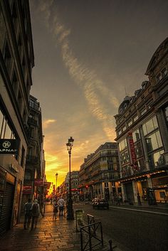 people walking down the street at sunset in an urban area with tall buildings on both sides