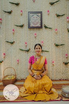 a woman sitting on the ground in front of a wall with pink flowers and birds