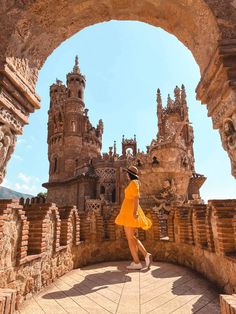 a woman in a yellow dress is walking through an archway to a castle like building