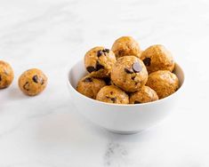 a bowl filled with chocolate chip cookies on top of a white marble counter next to three smaller ones