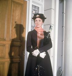 a woman standing in front of a door wearing a black dress and hat with white gloves