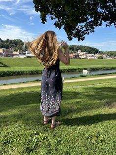 a woman standing on top of a lush green field next to a tree and water