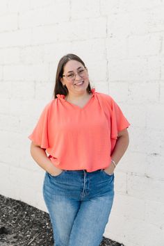 ALL SALES FINAL NOT ELIGIBLE FOR RETURN Get ready for some playful style with the Elliot Top! Made with light weight material, this top features a trendy v-neck mock ruffled neckline and adorable flutter sleeves. In a beautiful coral color, it's perfect for adding a pop of fun to any outfit. (Warning: May induce feeling of pure joy and compliments!) Fits true to size. Model is wearing a small and is 5'4". Plus model is wearing a 1X and is 5'5". Size Chart Length Bust S 27" 40" M 27" 42" L 27" 44 Chic Pink V-neck Top For Spring, Feminine Orange V-neck Top, Flowy Orange V-neck Blouse, Orange V-neck Blouse With Ruffles, Trendy Pink V-neck Top For Spring, Elliot Top, Tiered Dresses, Plus Model, Teen Dress