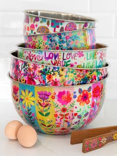 four bowls with colorful flowers and words painted on them, next to wooden spoons