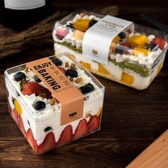 two desserts in plastic containers sitting on a table next to a bottle of wine