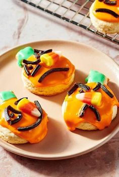 three decorated cookies sitting on top of a white plate next to a cooling rack filled with orange frosting