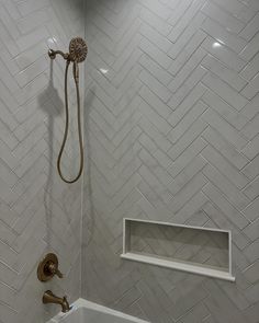 a bathroom with white herringbone tile and gold faucet in the shower head