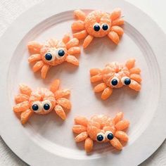 four orange crab cookies on a white plate with blue eyes and googly gums