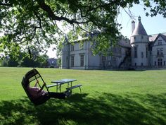 a bench and table in front of a large building with a big tree on the lawn