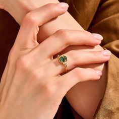 a woman's hand with a green ring on her left wrist and the other hand holding an emerald