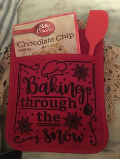 a red oven mitt with baking through the snow written in black on it and a spoon inside