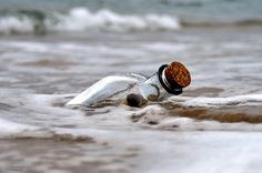 an empty bottle floating in the ocean on top of sand and water with waves coming up around it