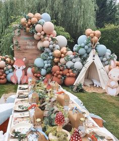 a table set up for a party with balloons and woodland animals on the wall behind it