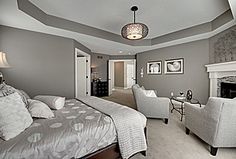 a bedroom with gray walls and white bedding, two chairs and a fireplace in the corner