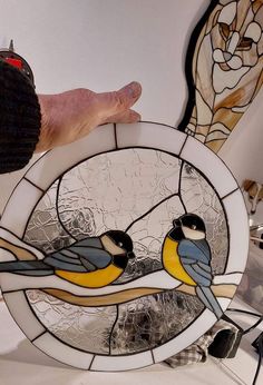 a hand holding a stained glass window with two birds on it and another bird in the background