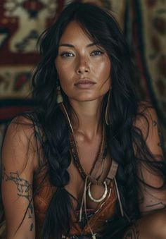 a woman with long black hair and tattoos on her chest sitting in front of a rug