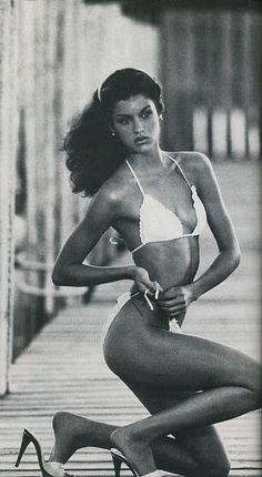 a black and white photo of a woman in a bathing suit with high heels on the ground