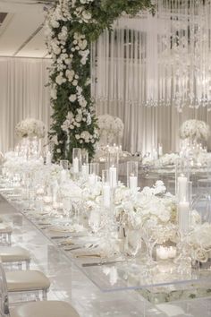 a long table with white flowers, candles and chandeliers on the wall behind it