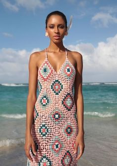 a woman is standing on the beach in a crocheted dress with feathers sticking out of her head