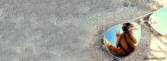 a pair of mirrored sunglasses with a woman's reflection on the side, sitting in the sand