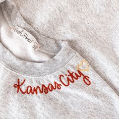 a gray sweatshirt with the word kansas embroidered on it's chest and an orange heart at the bottom