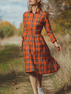 a woman in an orange plaid dress is walking down a path with her hair blowing in the wind