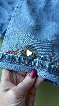 a woman's hand holding onto a pair of jeans with embroidered flowers on them