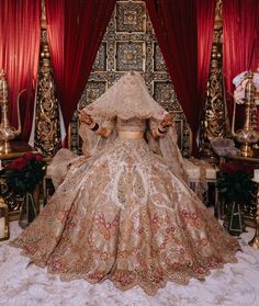 an elaborately designed wedding gown sits in front of red drapes and gold chairs