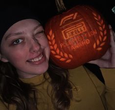 a woman is holding up a carved pumpkin