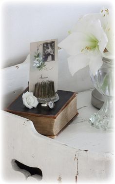 a vase with white flowers and an old book on a small table in front of it