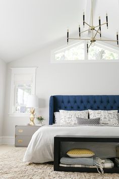 a bedroom with white walls and blue upholstered headboard on a bed in front of a window