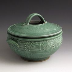 a green pot with a handle on the top and an ornate design on the bottom