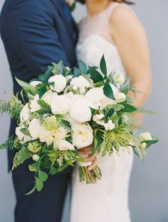 a bride and groom pose for a wedding photo with white flowers in their bouquets