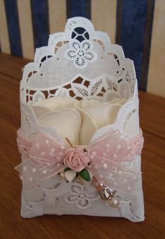 a small white box with pink roses and pearls on it sitting on a wooden table