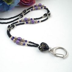 a black beaded necklace with purple beads and silver clasp on a white table next to flowers