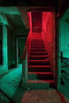 an abandoned building with red stairs leading up to the exit way and green light coming from the ceiling