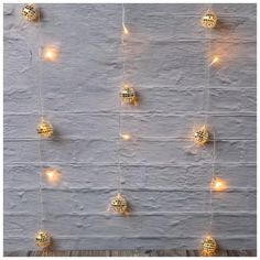 some lights are hanging from the side of a wall with balls on it and one light is turned on