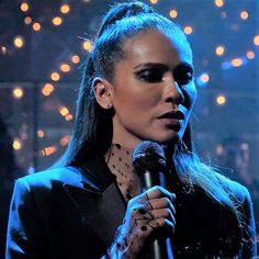 a woman holding a microphone in front of a christmas light filled room with lights behind her