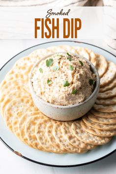 a white plate topped with crackers and a bowl of fish dip surrounded by crackers