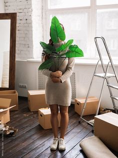 a woman holding a plant in her hands while standing next to boxes and ladders