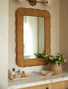 there is a vase with flowers on the counter in front of a mirror and vanity