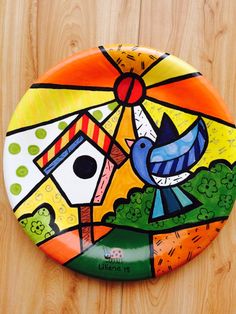 a colorful plate with a bird on it sitting on top of a wooden table next to a wall