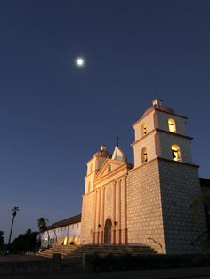 an old church lit up at night with the moon in the sky