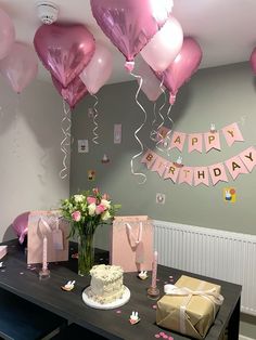 a birthday party with pink balloons and gifts on the table, along with cake and flowers